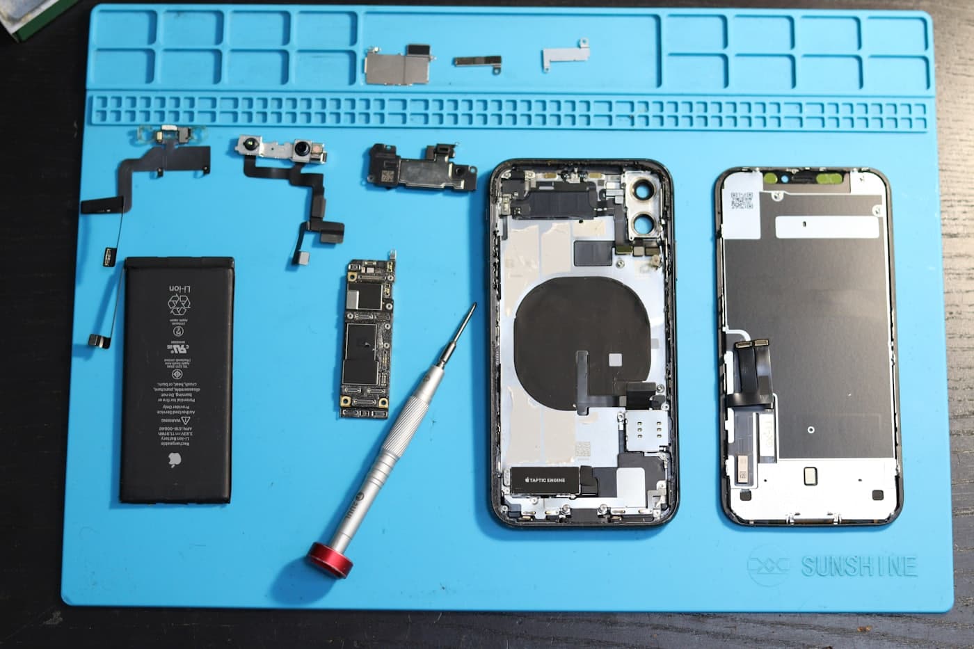 Smartphone entièrement démonté sur un tapis d'atelier : batterie, carte mère, écran et outils de précision