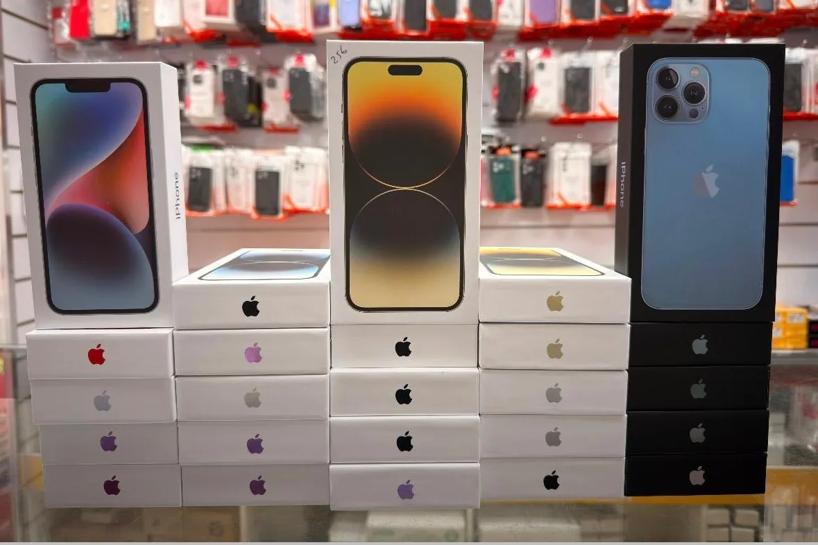 Téléphones neufs sous blister empilés sur le comptoir de SAV Smartphone, devant le mur de coques et de protections